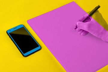 Colour Blocking Artwork, table with mobile phone, writing pad and one hand with pen in hand 