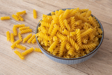 uncooked pasta in a white and dark blue stripe bowl with wood like background
