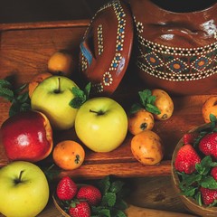 closeup of fruit arranged on a wooden table in a rustic composition with ethnic vase and wrapped in a warm light