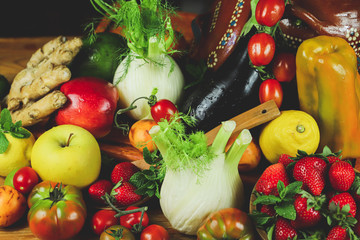
closeup of fruit and vegetables arranged on a wooden table in a rustic composition and wrapped in a warm light