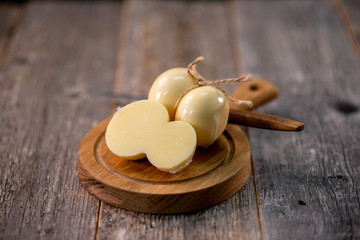 Medium hard cheese head scamorza on wooden board with knife wooden texture daylight