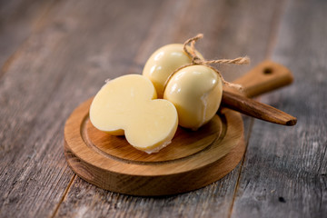 Medium hard cheese head scamorza on wooden board with knife wooden texture daylight