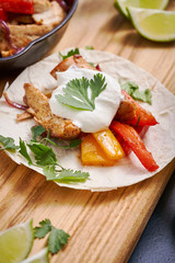 Close up shot of a tortilla with fried chicken and pepper stuffing on a wooden board