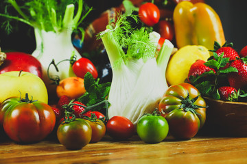 
closeup of fruit and vegetables arranged on a wooden table in a rustic composition and wrapped in a warm light
