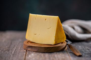 Medium hard cheese head edam gouda parmesan on wooden board with knife wooden texture daylight - obrazy, fototapety, plakaty