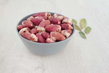 Raw chicken hearts in blue bowl with aromatic spices - bay leaves, on white wooden background with copy space