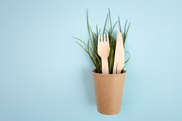 Eco-friendly disposable utensils made of bamboo wood on blue background. Go green, save environment concept . Eco-friendly biodegradable paper cups with bamboo fork and knife on a blue background