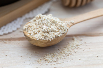 Hazelnut flour in a wooden spoon on a white table.