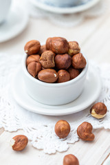 Fresh organic hazelnuts in a white cup on a white table.