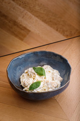 Tasty pasta with white sauce topped with mint leaves on blue bowl in wooden table background. Photography best use for commercial magazine or restaurant’s book menu.