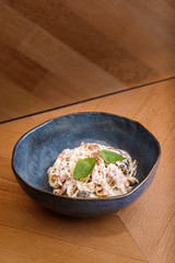 Tasty pasta with white sauce and veggies topped with mint leaves on blue bowl in wooden table background. Photography best use for commercial magazine or restaurant’s book menu.
