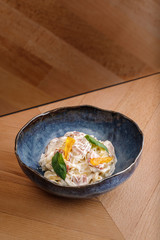 Tasty pasta with white sauce thin sliced bacon topped with mint leaves on blue bowl in wooden table background. Photography best use for commercial magazine or restaurant’s book menu.
