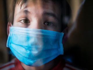 Boy with a medical mask looks sadly out of the window during his confinement because of convid 19