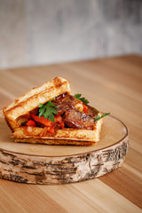 Presentable plating of Belgian waffle topped with red eat and sauce  on a nice cut wooden chopping board. Food photography concept for magazine or online delivery menu.