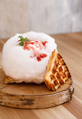 Chocolate waffle topped with cotton candy and vanilla ice cream glazed with strawberry syrup presentable plating on a nice wooden chopping board. Sweet photography concept for magazine.