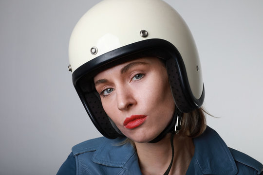 Close-up portrait of biker young woman, wearing white helmet, with red lips. Studio background.