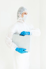 Naklejka premium a man in a protective suit, gloves and face mask is Walking with a suitcase for tests in his hands. The concept of combating coronavirus. Isolated on a white background
