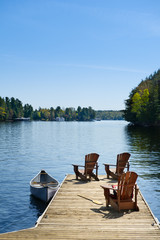 Three Adirondack chairs on a wooden dock on a calm lake in Muskoka, Ontario Canada. Tied to the...