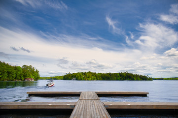 Lake view from a cottage wooden dock in Muskoka, Ontario Canada. A small motorboat is leaving the...