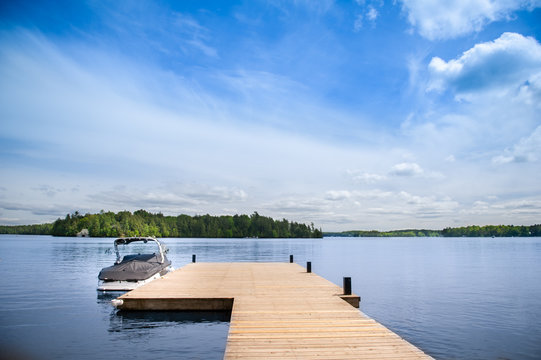 Fototapeta Cottage lake view with boat docked on a wooden pier in Muskoka, Ontario Canada.