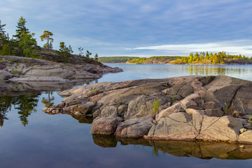 Obraz premium Lake with rocky shores. Pine trees grow on the stone banks. Islands of stone. Calm natural landscape. Rocky Islands in the water.