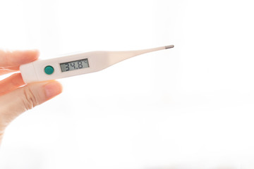 The fingers of a female hand hold an electronic thermometer with a temperature of 34.8 degrees on a scoreboard on a white background. Pathology, disease, hypothermia.