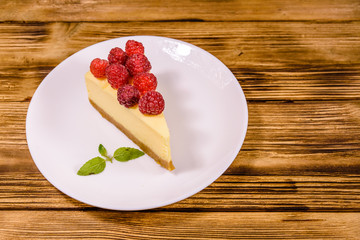 White plate with cheesecake New York, leaf of mint and raspberries on wooden table