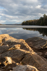 Boulders on the shore of Smoke Lake in Algonquin Park in Spring with clouds reflecting in the glassy water