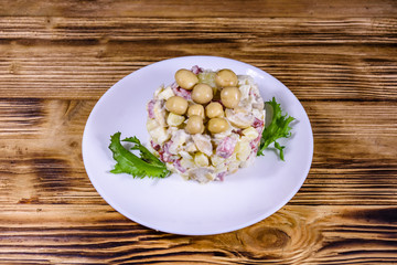Salad with marinated mushrooms, sausage, onion, boiled potato and mayonnaise on a wooden table