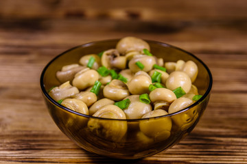 Glass bowl with canned mushrooms and green onion on wooden table