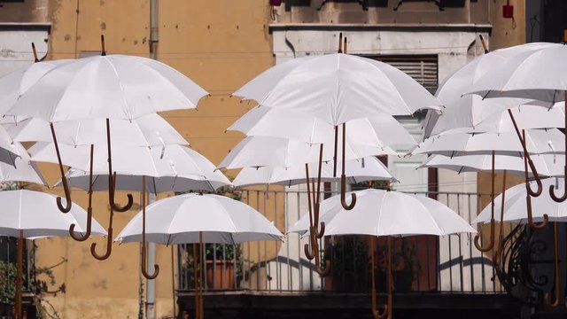 White umbrellas are hanging on rope between old buildings, swaying by the wind. Umbrella Sky Project. Catania, Sicily, Italy. Close up