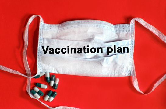 VACCINATION PLAN - text on a protective face mask, tablets on a red background