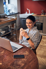 Pretty Caucasian lady smiling opposite laptop in cozy room