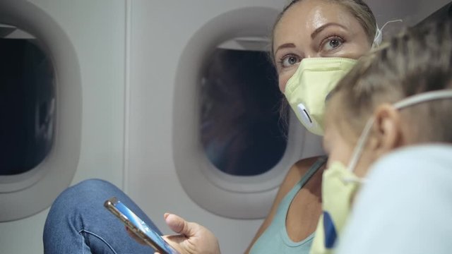 Family woman and child baby travel tourist caucasian at plane aircraft with wearing protective medical mask. Use smartphone mobile. Health virus protect coronavirus epidemic sars-cov-2 covid-19.