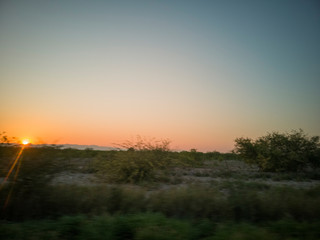 Fototapeta na wymiar Atardecer. o amanecer a un lado de la carretera tomadas con el vehículo en marcha, algunos árboles al fondo, cielo azul.