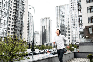 Get in shape. Young man in sportswear runs outdoors among the city skyscrapers