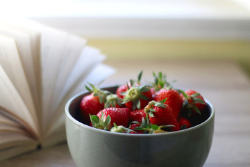 Bowl of fresh strawberries and open book. Selective focus.