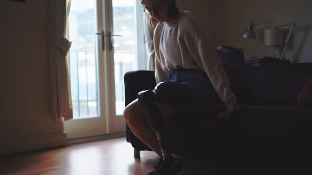 Young woman taking off her artificial leg at home