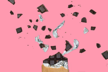 Explosion Of Broken Chocolate on Pastel Pink Background With Chocolate Chunks and Parts of Foil. Sweet Tooth