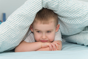 offended little boy lays under the blanket and looks down
