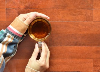 Cups of hot tea in hands of women on wooden floor background with copy space for text, top view with selective focus​ on​
