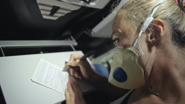 Woman travel caucasian at plane with wearing protective medical mask. Girl tourist at aircraft with protect respirator, fill out a registration form about her health. Coronavirus sars-cov-2 covid-19.