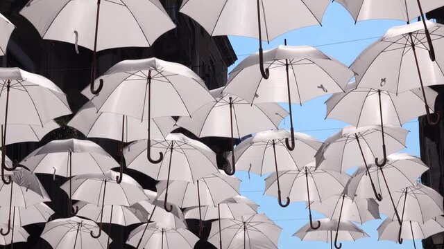 White umbrellas are hanging on rope between old buildings, swaying by the wind. Umbrella Sky Project. Catania, Sicily, Italy. Close up