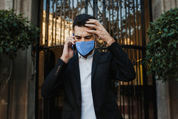 worried man wearing face mask against contagious coronavirus and talking by phone outside in street