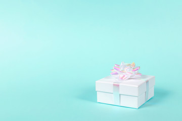 Obraz premium White gift box with holographic bow on pastel blue background. Shot at angle. Copy space