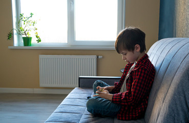 Focused boy enthusiastically plays in a smartphone. Leisure during self-isolation concept. Gadget...
