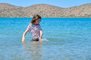 Fototapeta na wymiar Teenager girl is touching, enjoying sea water in the bay