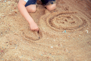 Kid's hand drawing on the sand at the seacoast, top view, copy space. Summer mood