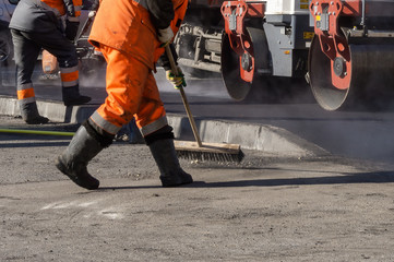 during the renovation of old asphalt, road workers in orange uniforms prepare surfaces for paver operation