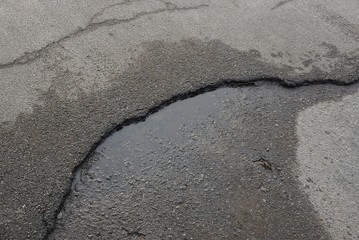 stone texture of gray wet asphalt on a black cracked road